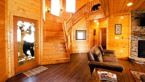 Un intérieur en bois avec un escalier, un canapé, une cheminée et un ours visible à travers une porte en verre.