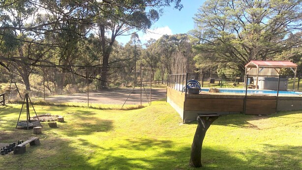 Un espacio al aire libre cercado con una estructura de madera, posiblemente un área de juegos o un refugio para picnic, y una piscina al fondo.