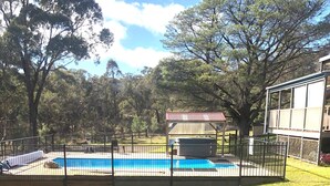 Una piscina cercada con jacuzzi, rodeada por un césped y árboles.