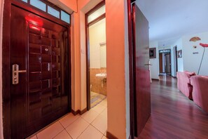 Un pasillo con una puerta de madera, un baño con lavamanos y un sofá rosa en la sala de estar.