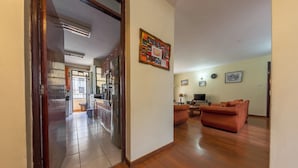 A living room with a sofa, a coffee table, and a TV. There is a kitchen in the background with cabinets and a refrigerator. - Takdiri Home Superior (Nairobi)