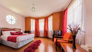 A bedroom with a bed, a desk, a chair, a vase with dried plants, a window with curtains, and a wall clock. - Takdiri Home Superior (Nairobi)