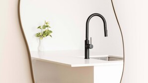 Una cocina con encimera blanca, grifo negro y dos taburetes de mimbre.