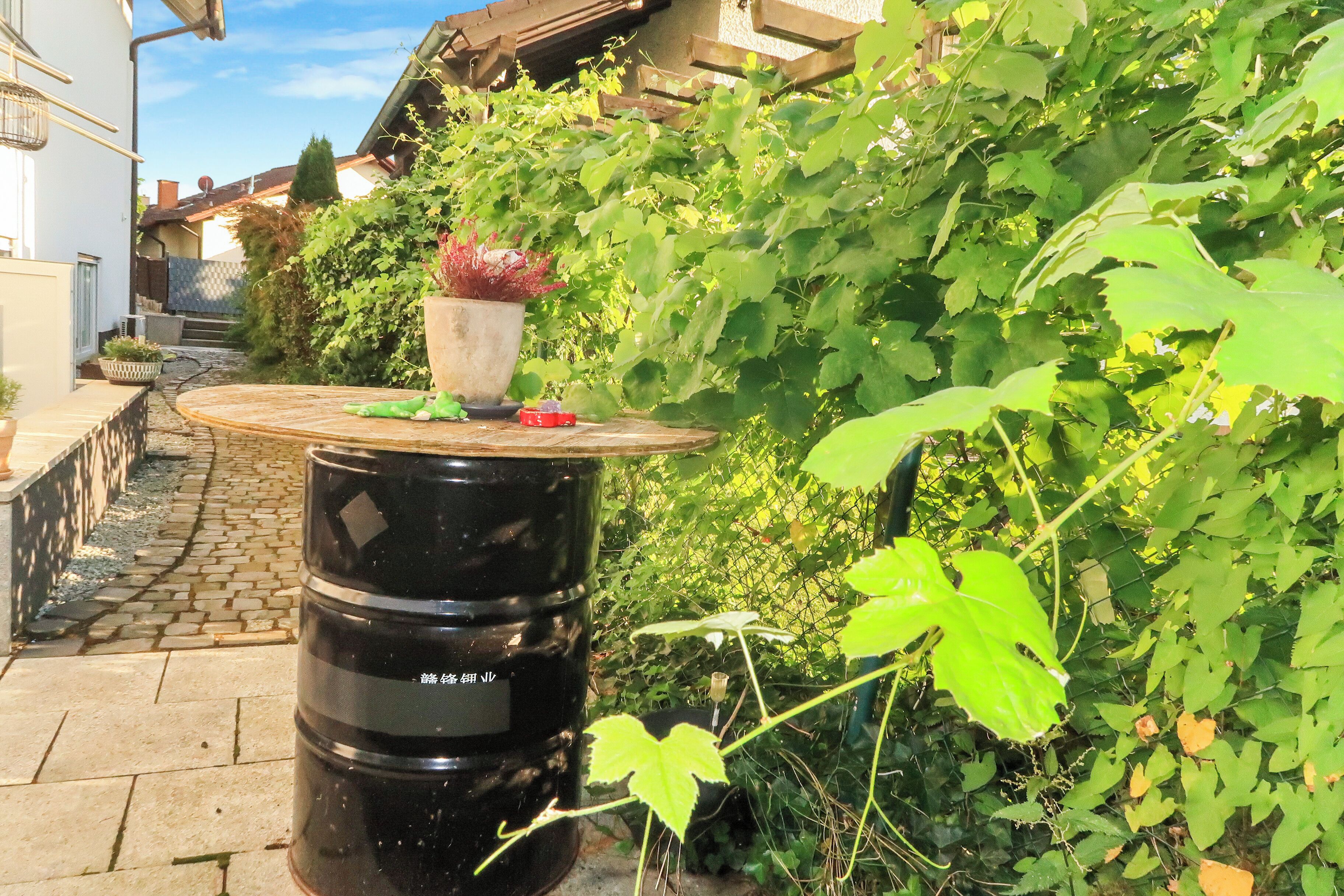 A garden area with a round table, potted plants, and a black barrel.