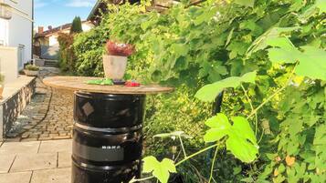 A garden area with a round table, potted plants, and a black barrel.