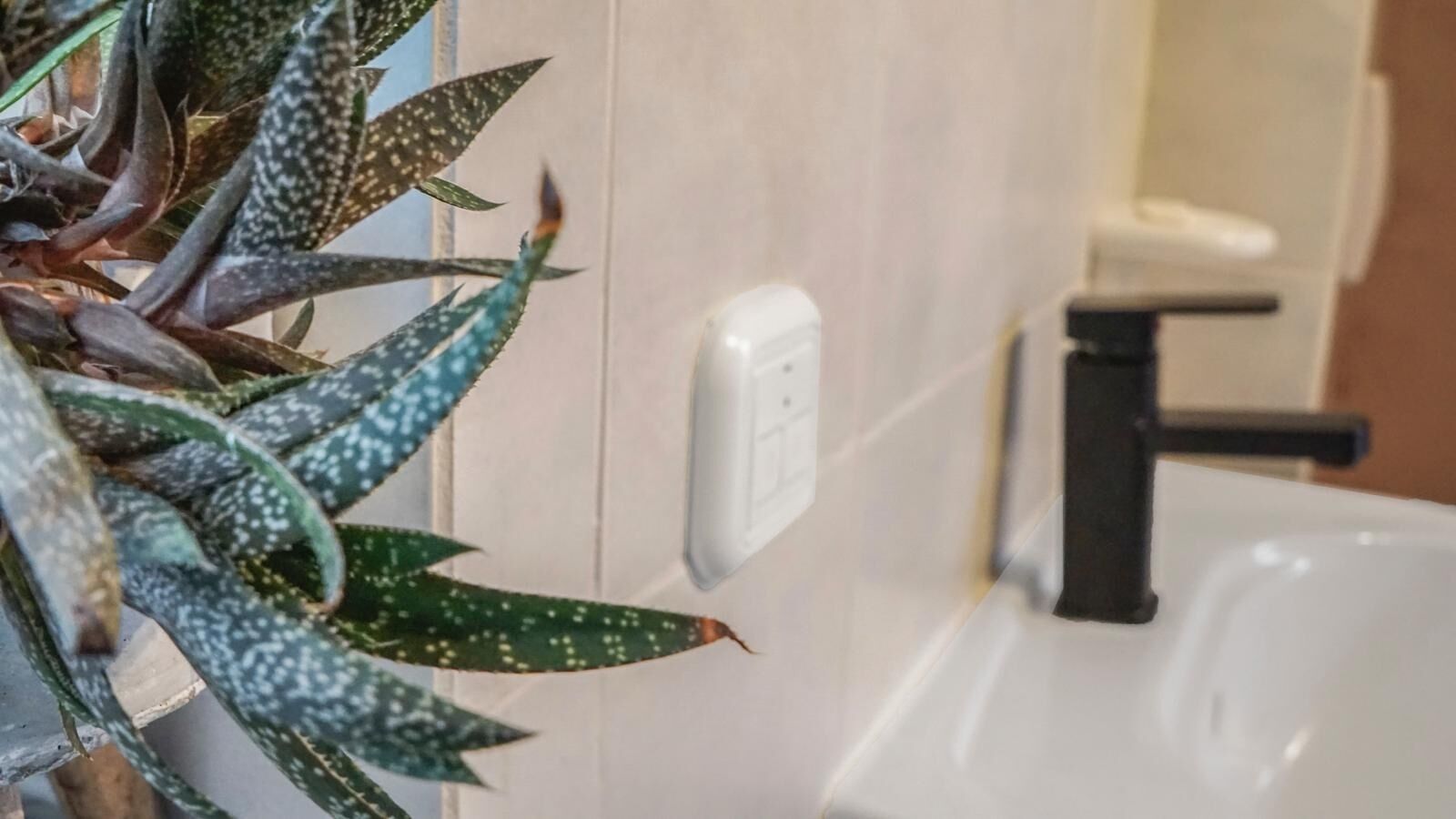 A bathroom with a white sink, a black faucet, and a wall-mounted light switch.