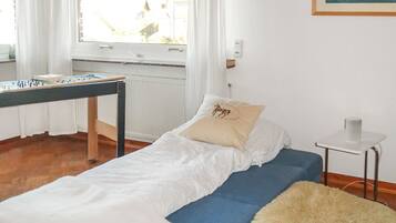 A room with a bed, a small table, a window with curtains, and a painting on the wall.