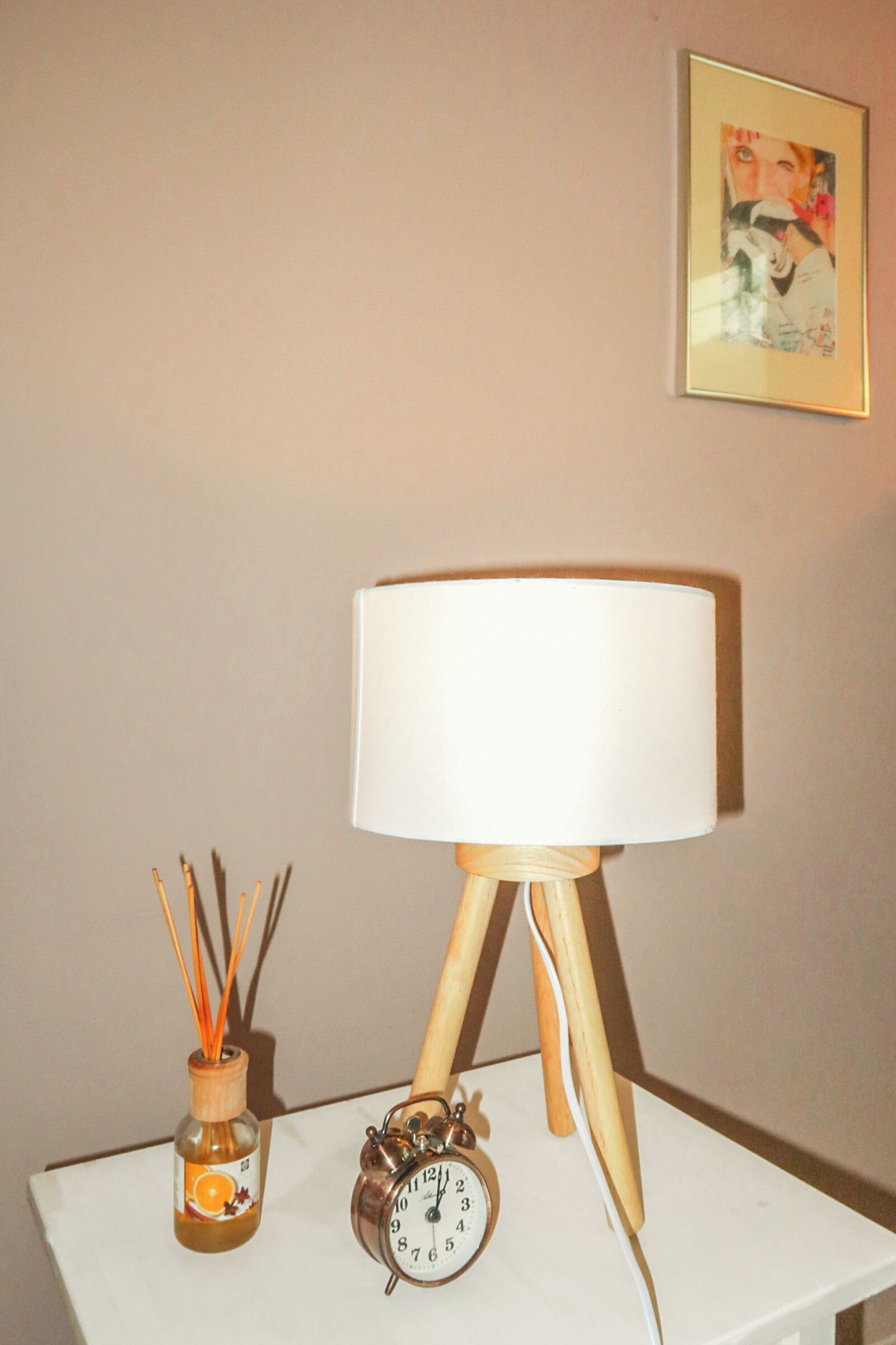 A table with a white lamp, an alarm clock, and a bottle of scented oil.