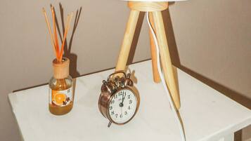 A table with a white lamp, an alarm clock, and a bottle of scented oil.