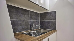 Een keuken met een houten aanrecht, een roestvrijstalen spoelbak en donkergrijze tegels.