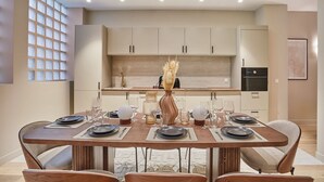 Un espace repas moderne avec une table en bois dressée pour six personnes, une cuisine en arrière-plan et une grande fenêtre à carreaux.