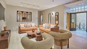 Un salon spacieux comprenant un ensemble de canapés, deux fauteuils, une table basse et une grande fenêtre laissant entrer la lumière naturelle.