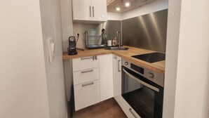 A compact kitchen with white cabinets, a wooden countertop, a built-in oven, and a coffee maker. - Renovated Apartment in Seignosse Penon - Walk to Beach & Shops, Free Parking, Wi-Fi (Seignosse)