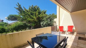 A balcony with a table and chairs, a potted plant, and a view of trees and buildings. - Renovated Apartment in Seignosse Penon - Walk to Beach & Shops, Free Parking, Wi-Fi (Seignosse)