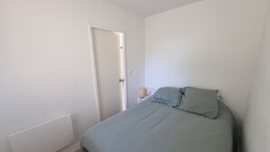 A bedroom with a bed, a nightstand, and a door. - Renovated Apartment in Seignosse Penon - Walk to Beach & Shops, Free Parking, Wi-Fi (Seignosse)