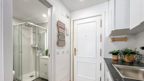 A narrow bathroom with a glass shower enclosure, a white door, and a sink with a dark countertop.