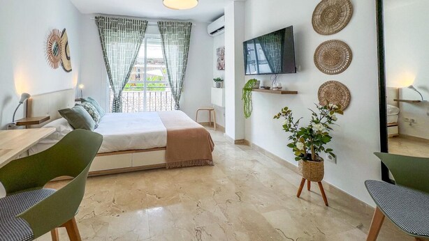 A modern bedroom with a bed, a desk, chairs, a TV, and decorative items.