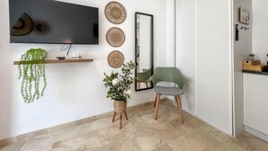 A modern living room with a flat-screen TV, a mirror, a green chair, and a small plant on a shelf.