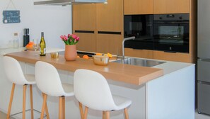 A modern kitchen with a central island, white bar stools, a stainless steel sink, and wooden cabinets.