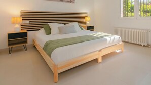 A modern bedroom with a wooden bed frame, white bedding, and two bedside lamps. - Large house, pool, AC, parking - 13 guests (Vall-llòbrega)