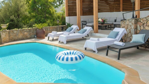 A swimming pool with lounge chairs and a floating ring, surrounded by stone walls and greenery.