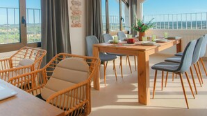 A dining area with wicker chairs, a wooden table, and a view of the landscape through large windows. - Large house, pool, AC, parking - 13 guests (Vall-llòbrega)