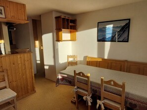 A room with a wooden bed, a small table, and a chair. There is a wooden cabinet and a framed picture on the wall.