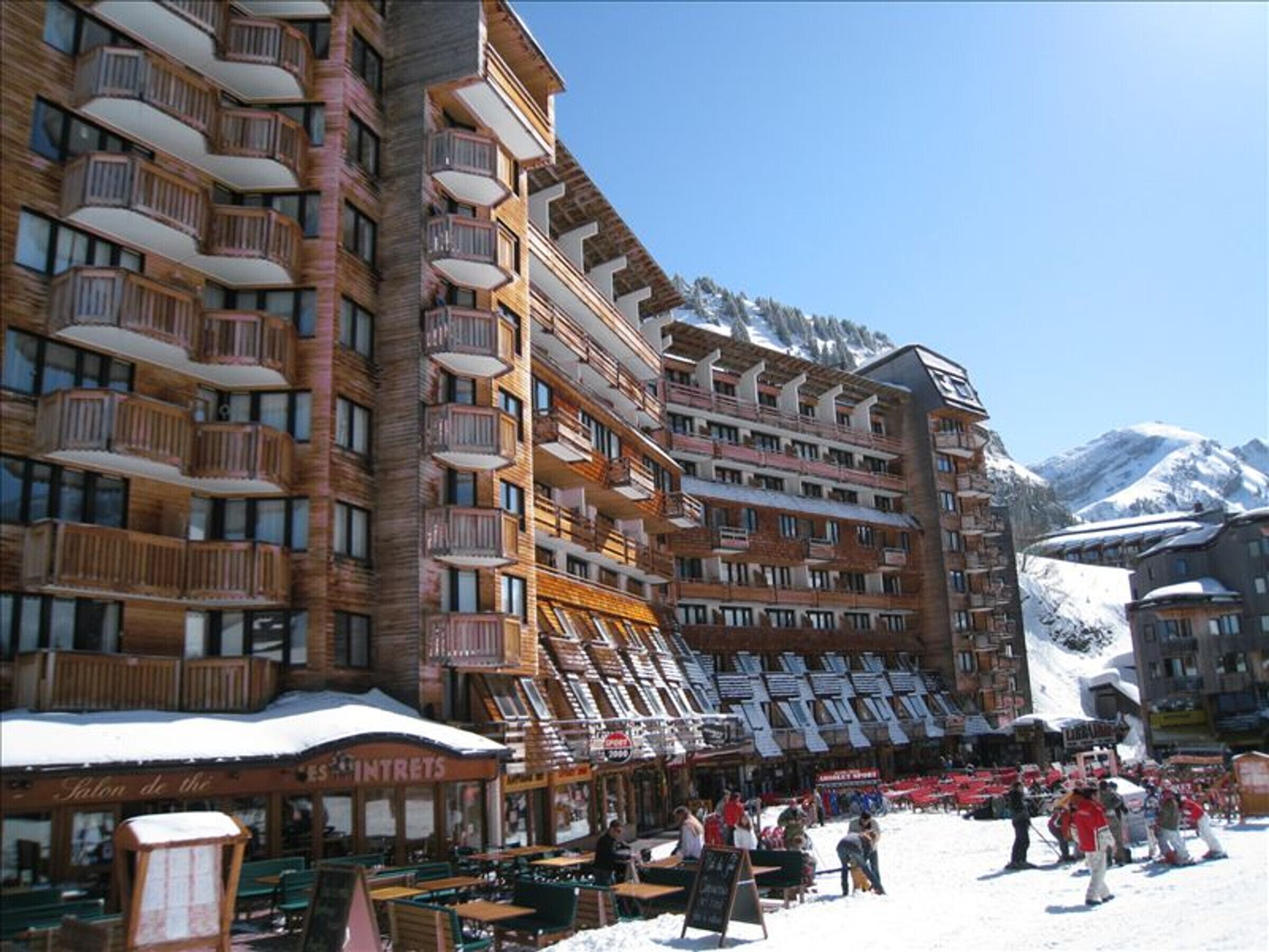 Een meerhoog hotel met balkons, een skigebied en een berg op de achtergrond.