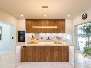 A modern kitchen with wooden cabinets, a marble countertop, and a central island with a fruit bowl. - Elegant Villa - 2 Bedrooms, Private Pool in Anse Marcel (Saint-Martin)