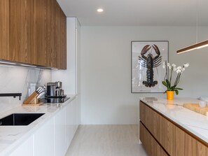 A modern kitchen with white cabinetry, a wooden countertop, and a coffee machine.