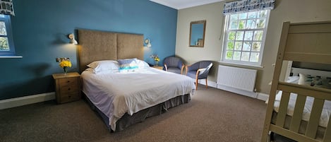 A bedroom with a large bed, bedside lamps, a chair, a window with a view, and a crib.