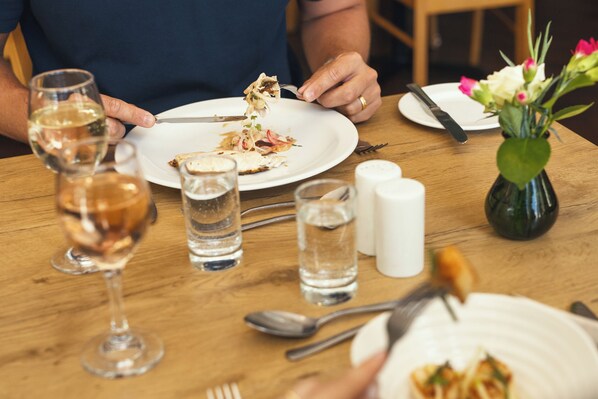 Une table à manger avec des assiettes, des couverts, des verres et un vase rempli de fleurs.