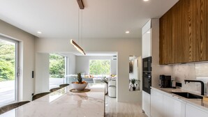 A modern kitchen with a marble island, wooden cabinets, and a view of the outdoors. - AURA 1 - Luxury with Private Pool and View in Anse Marcel (Saint-Martin)
