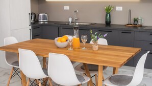 A modern kitchen with a wooden dining table, white chairs, and a bowl of oranges. - Three-Bedroom house with Jacuzzi & 2 Parkings (Vodice)