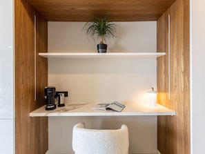 A modern room with wooden paneling, a white desk with a plant, a coffee maker, and a reading lamp. - Luxury and Serenity with Infinity Pool (Saint-Martin)