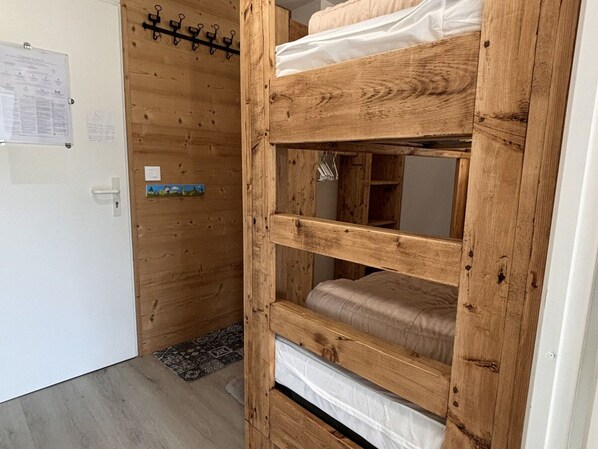 A bunk bed with wooden construction, a white door, and a bulletin board with notices.