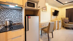 A compact kitchen with a microwave, kettle, and refrigerator. There is a dining area with a chair and a sofa.
