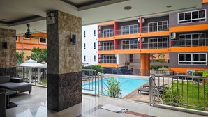 A modern hotel lobby with a pool area, outdoor seating, and a view of the building's exterior.