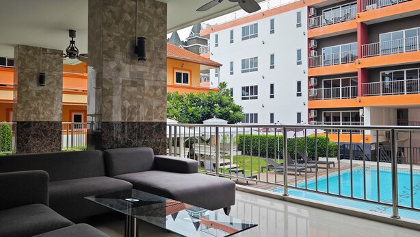A modern living area with a glass coffee table, grey sofas, and a view of a swimming pool and surrounding buildings.