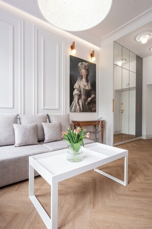 Una sala de estar moderna con un sofá blanco, una mesa de centro blanca con un jarrón de flores, y un cuadro grande en la pared.