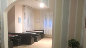 A spacious living area with a tiled floor, a black sofa, a dining table with chairs, and a potted plant. - Barone Beach Hotel (Rimini)