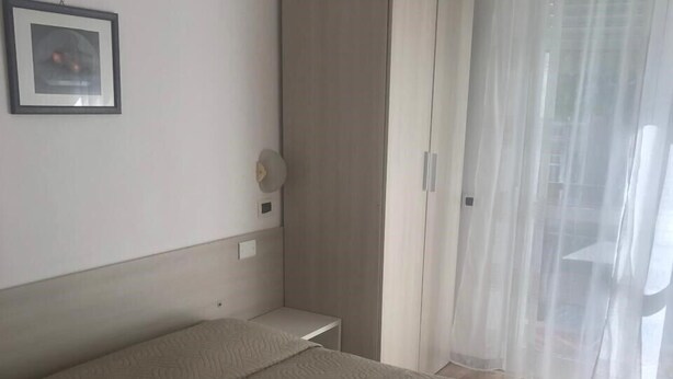 A hotel room with a bed, a wardrobe, a framed picture on the wall, and a window with sheer curtains. - Barone Beach Hotel (Rimini)