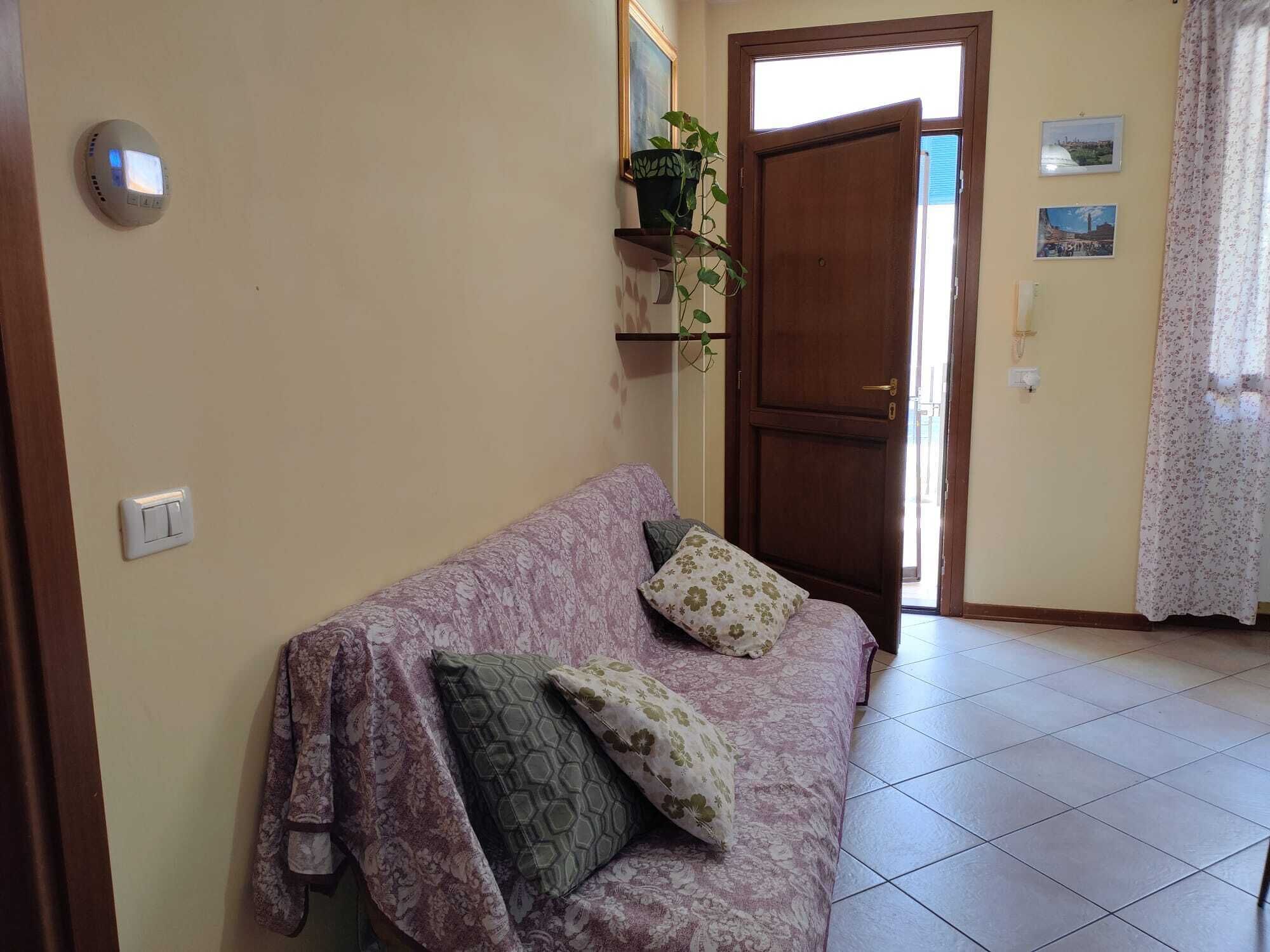 Un soggiorno con divano, una porta, una lampada a parete e una pianta in vaso.