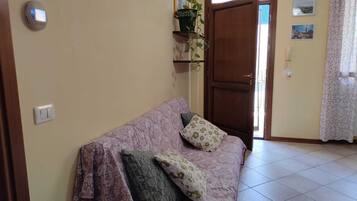 Un soggiorno con divano, una porta, una lampada a parete e una pianta in vaso.