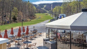 A terrace with outdoor seating, overlooking a forested valley and a ski slope.