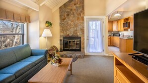 A living room with a stone fireplace, a sofa, a coffee table with flowers, and a television.