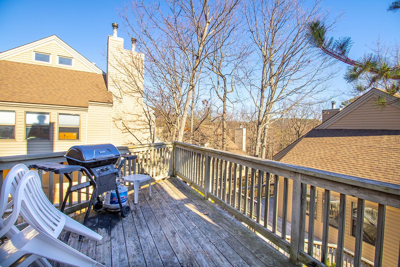 Une terrasse en bois avec un barbecue, une chaise en plastique blanche et une rambarde en bois.