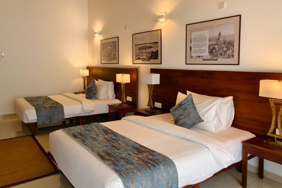 Habitación de hotel con dos camas, cabecero de madera, lámparas fijadas a la pared y cuadros enmarcados.