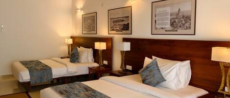 A hotel room with two beds, a wooden headboard, wall-mounted lamps, and framed pictures.