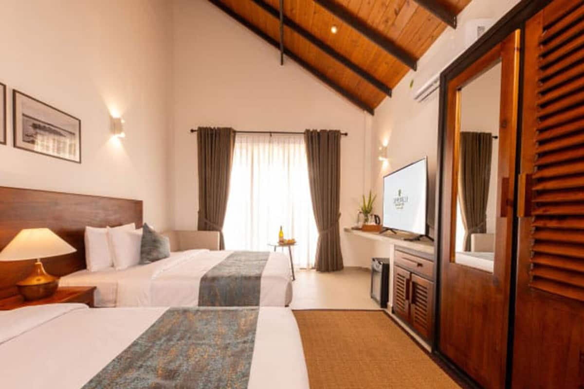 Habitación de hotel con dos camas, televisor, escritorio y un espejo grande.